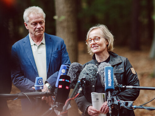 Zwei Personen stehen im Wald vor Mikrofonen.