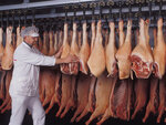 Fleisch hängt an einem Schienensystem eine Person in weißer Kleidung schiebt eine Reihen Keulen
